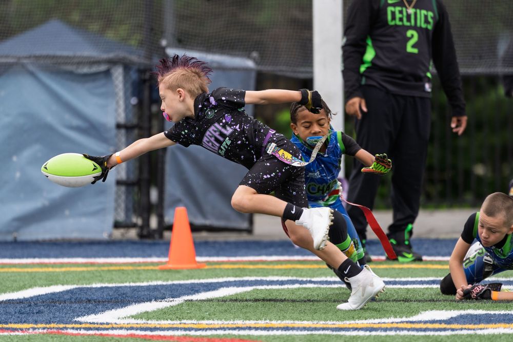 Young football player dives while reaching for the ball during an intense youth flag football game on turf field.