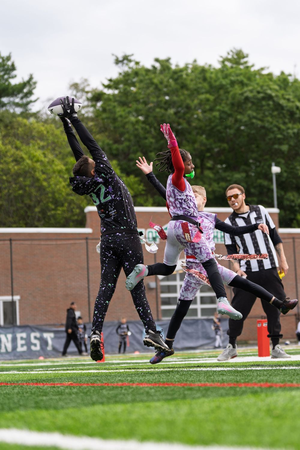 Two players in colorful uniforms leap high to catch a football while a referee watches during a competitive game.