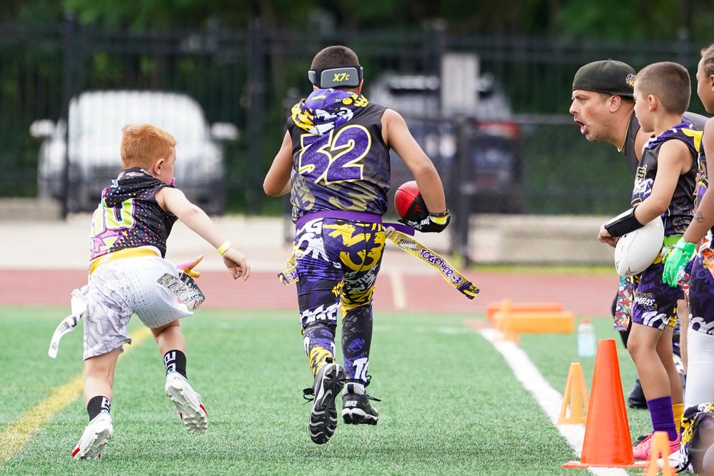 Young athlete jumps over training cone during youth football practice drill on turf field.
