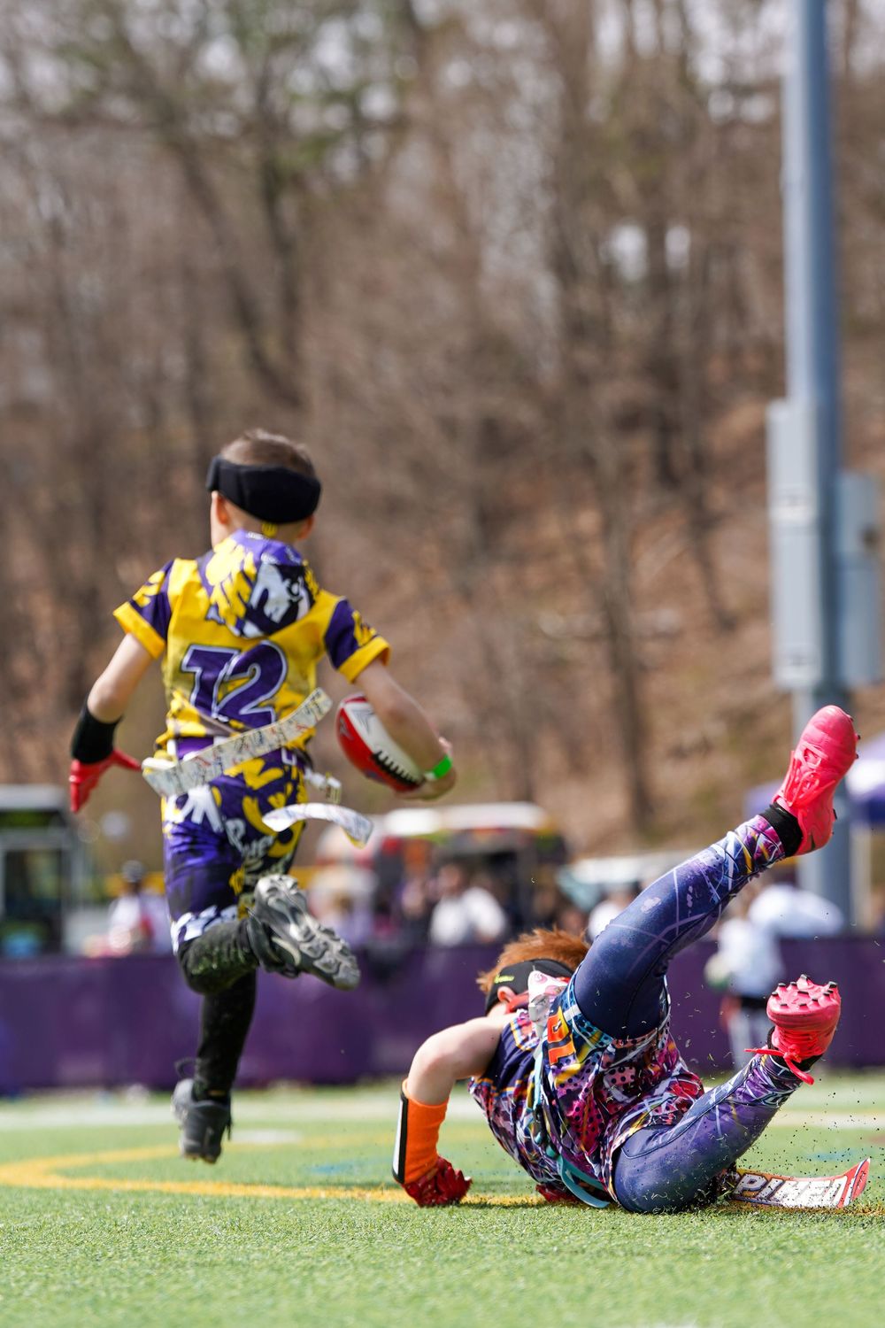 Two ultimate frisbee players in purple and yellow uniforms compete for the disc on a turf field during a game.