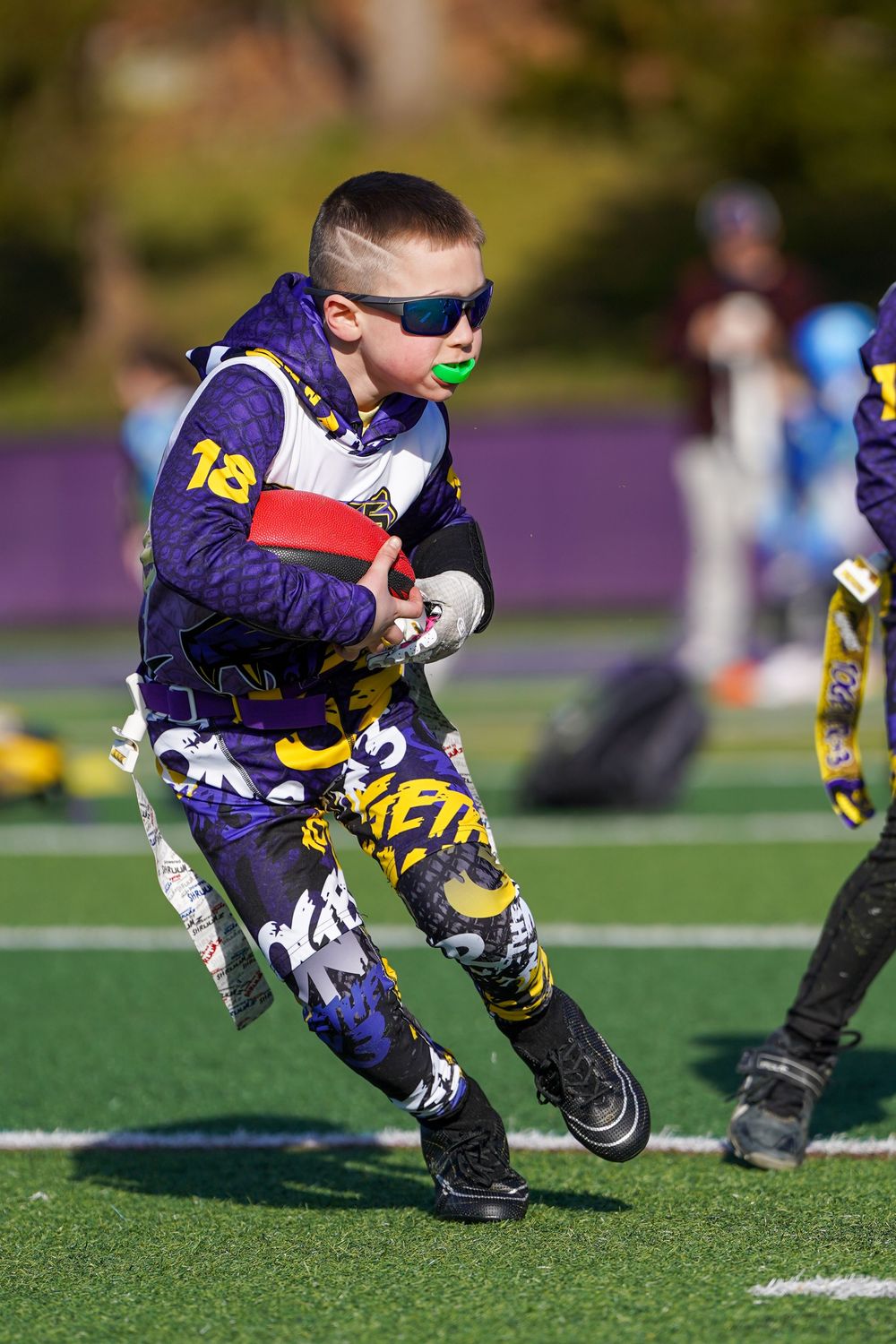 Young football player in purple jersey diving to make a low tackle during a game on artificial turf field.
