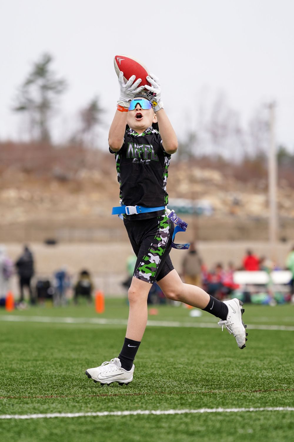 Ultimate Frisbee player in black shirt and green shorts leaps high to catch a red disc during outdoor competition.