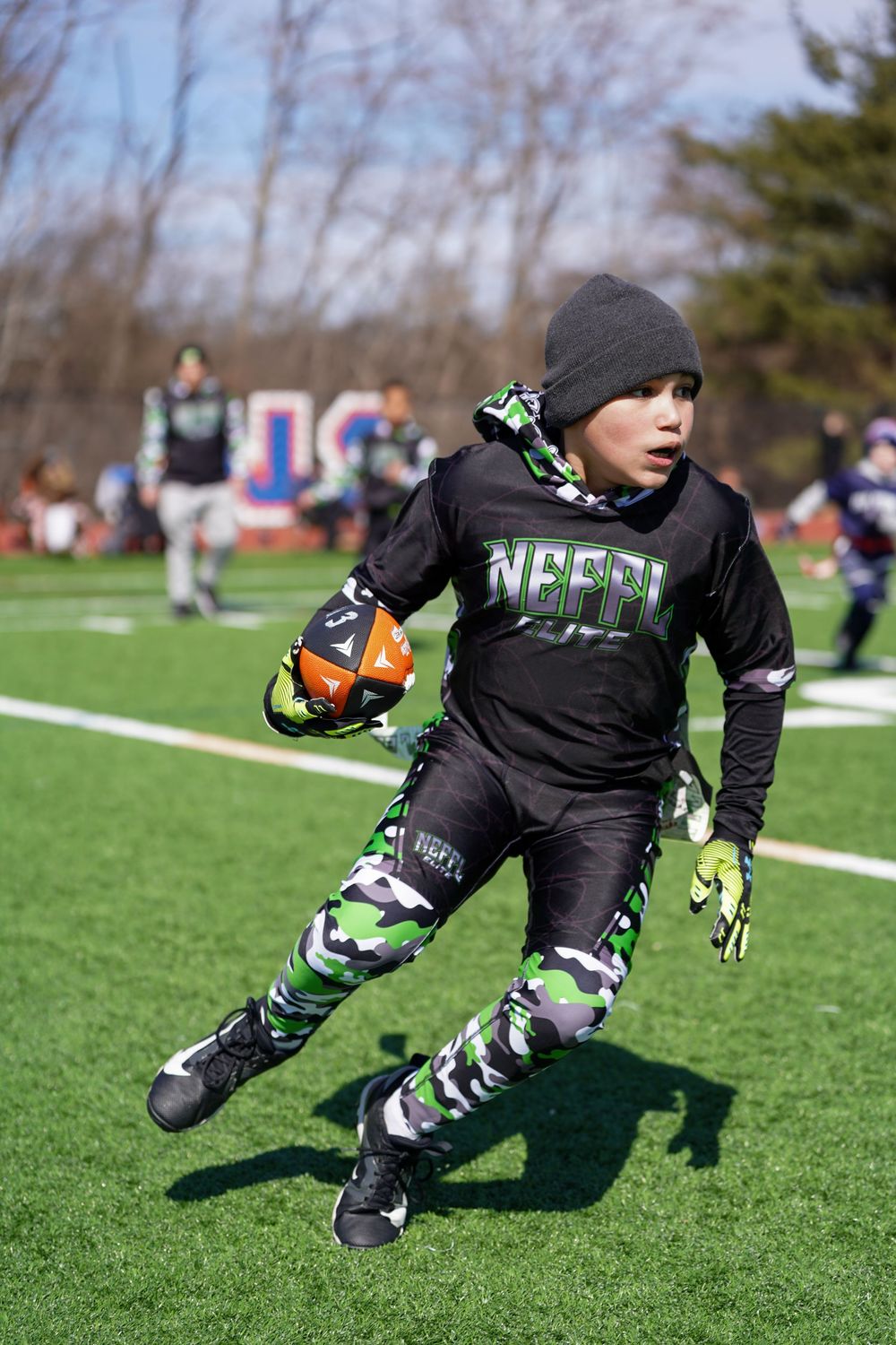 Football player in black uniform performs diving catch sequence on artificial turf field during training session.