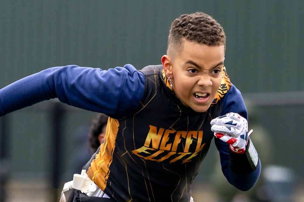 An athlete wearing a navy and gold jersey performs a dynamic running drill on a sports field.
