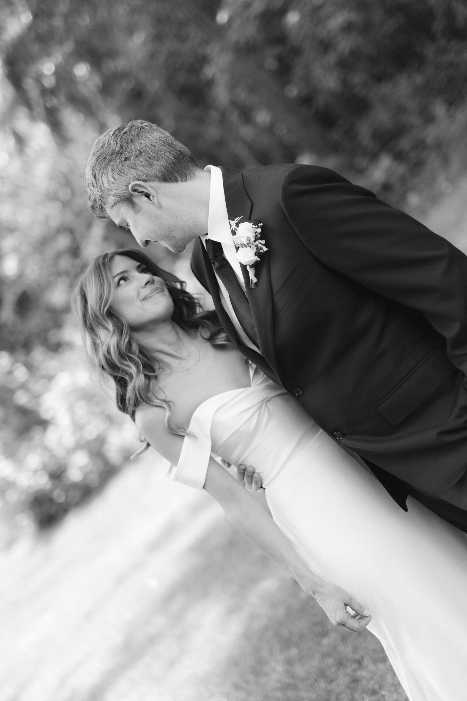 A black and white romantic wedding photo of a couple sharing an intimate moment in an outdoor garden setting.