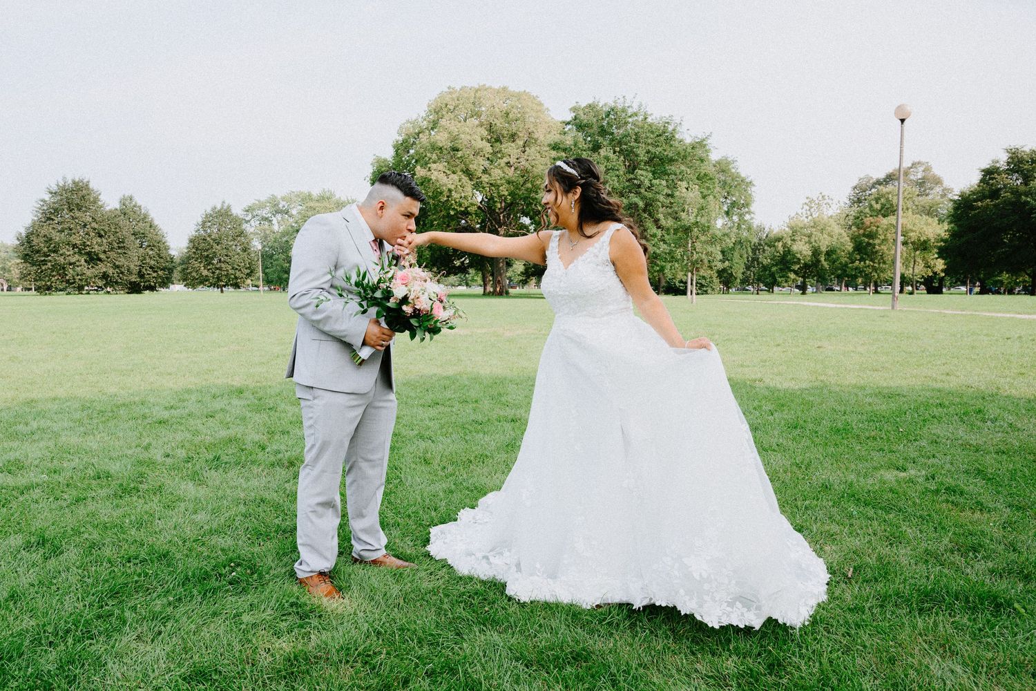 A couple in wedding attire share a playful moment on a green lawn during their summer celebration.