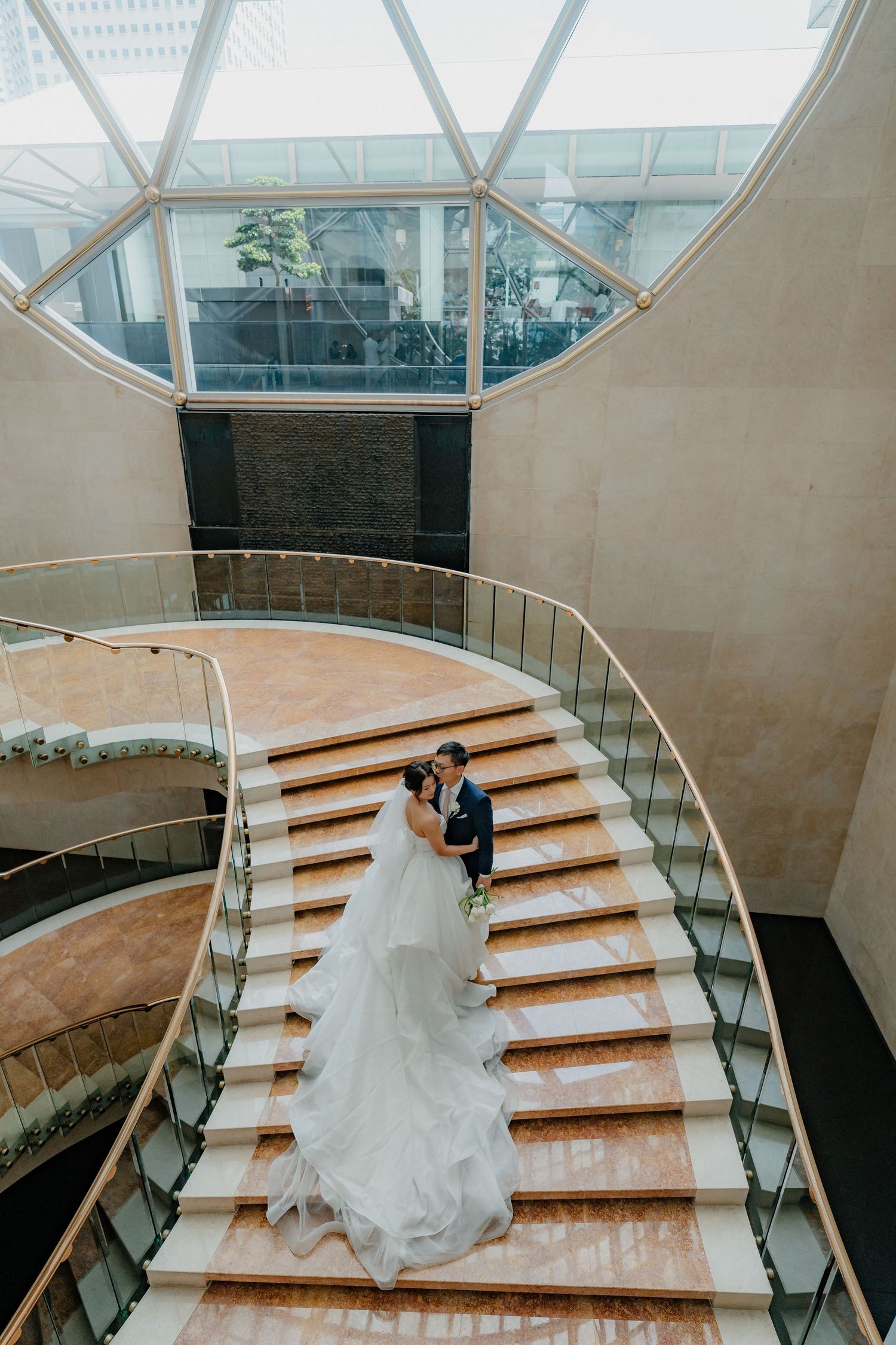 A grand sweeping staircase in a modern building with a long flowing white dress trailing down the wooden steps.