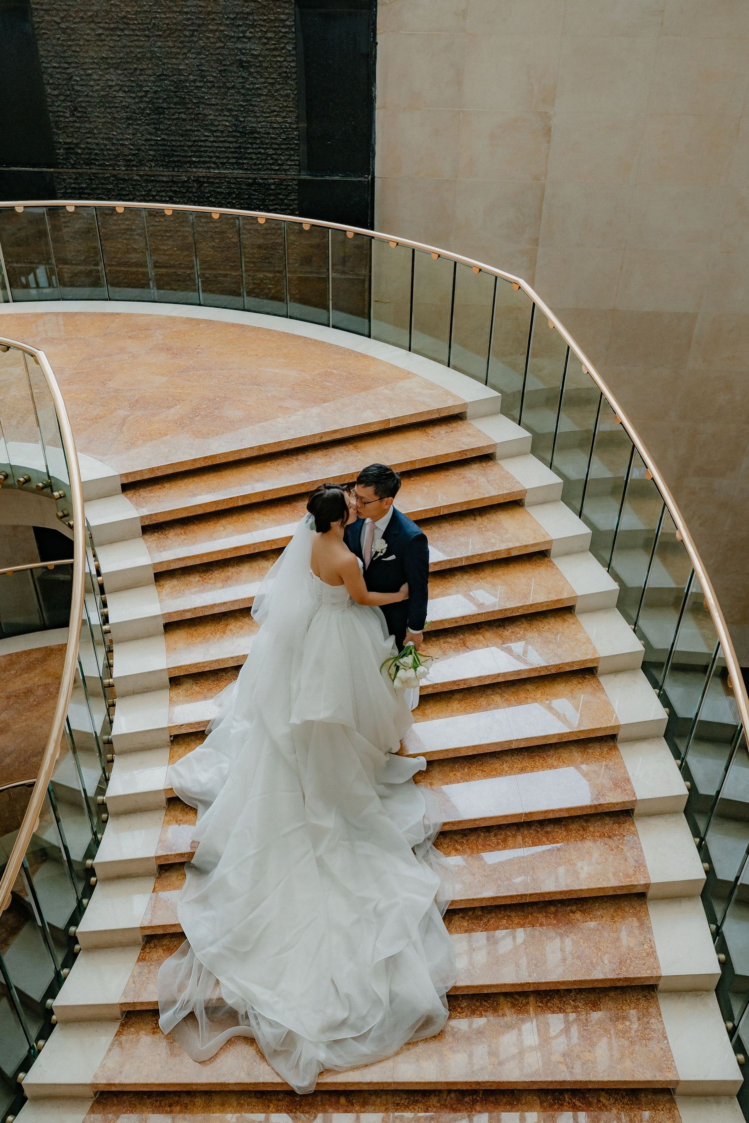 Flowing white wedding dress cascades down elegant marble stairs in an artistic wedding portrait series.