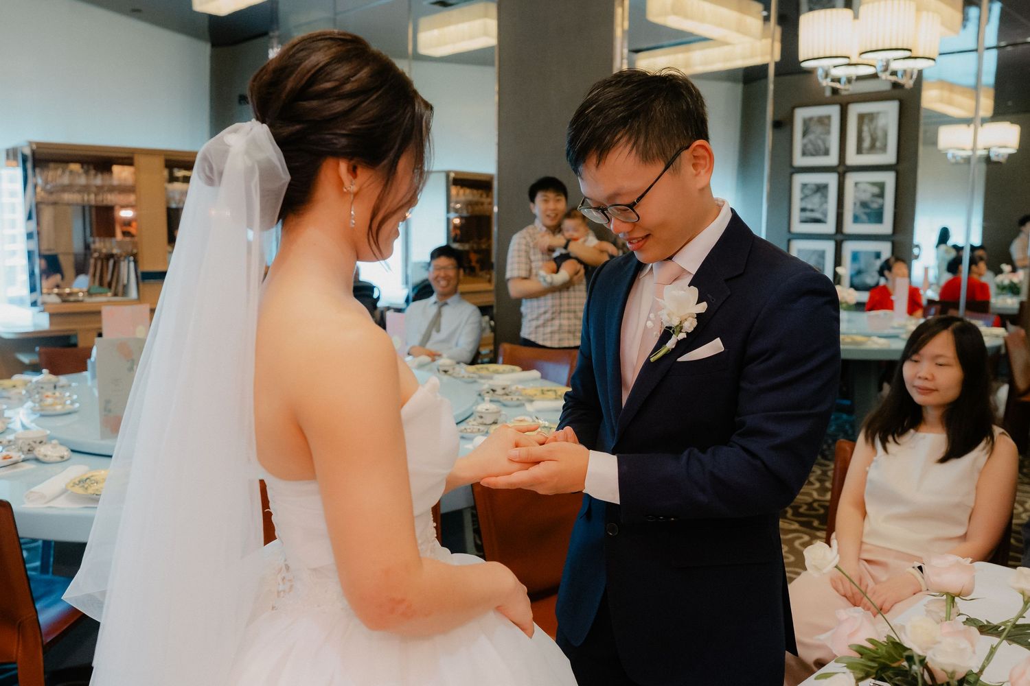 A couple exchanges rings during their wedding ceremony at an indoor reception venue decorated with blue accents.