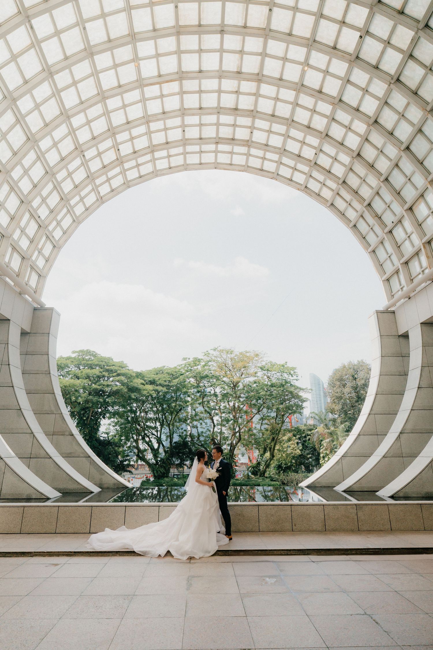 A wedding scene unfolds beneath an elegant curved white architectural structure.