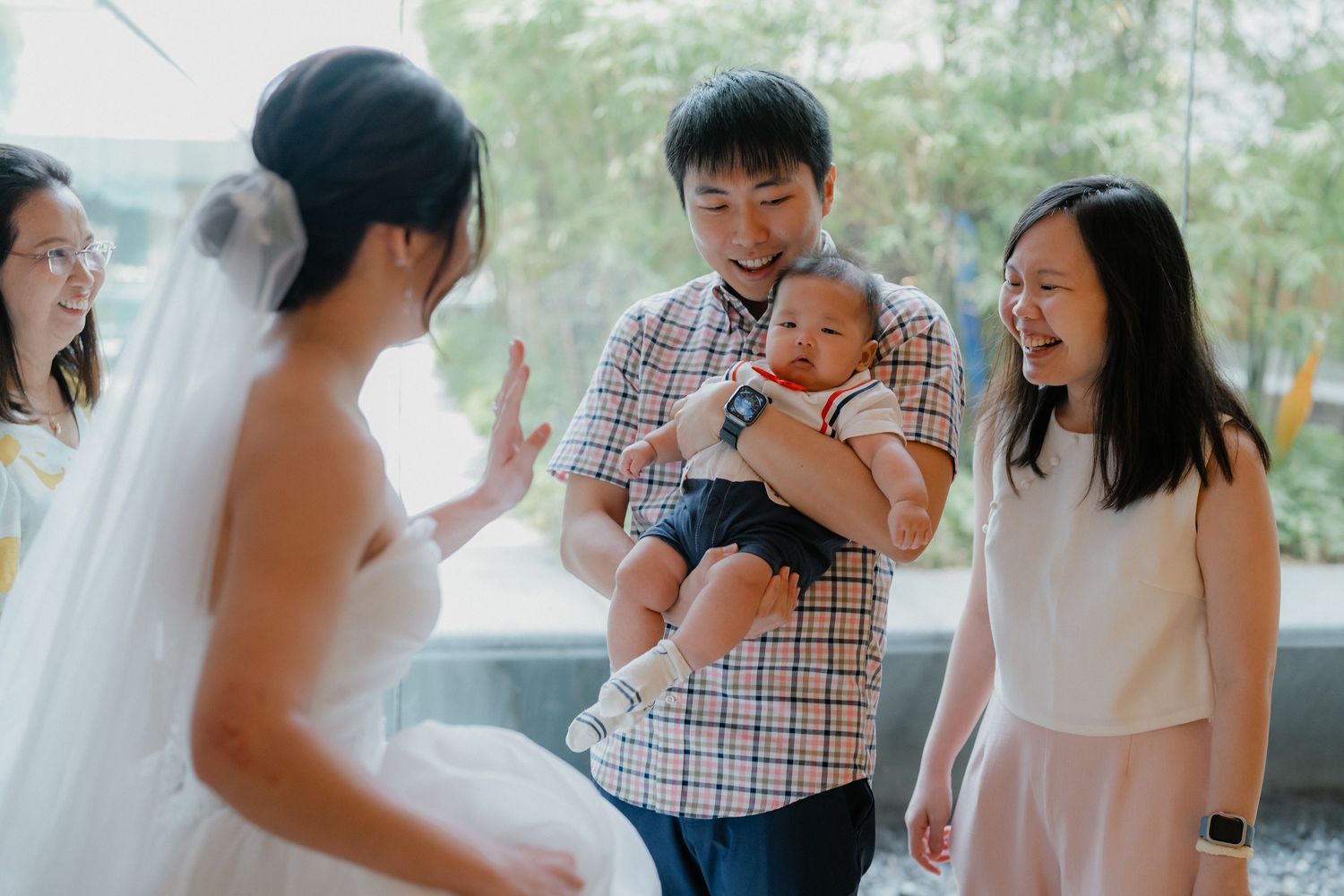 A group of wedding guests admire a bride in her gown while a toddler smiles during an intimate gathering.