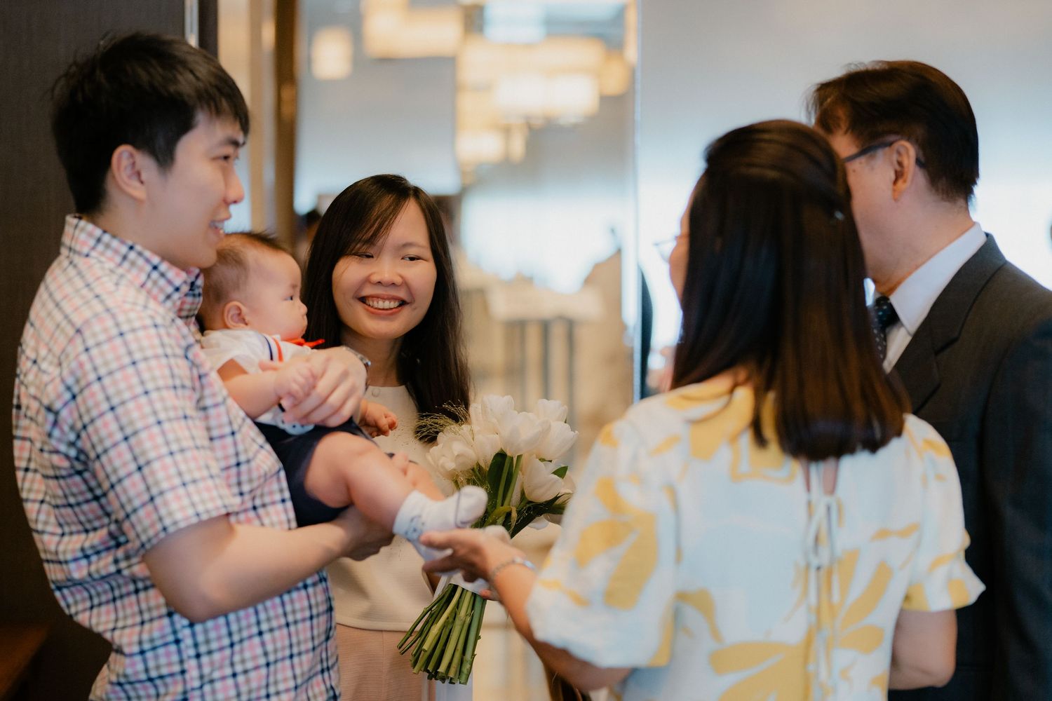 Several people gathered in a casual indoor setting sharing bouquets of flowers and engaging in conversation.