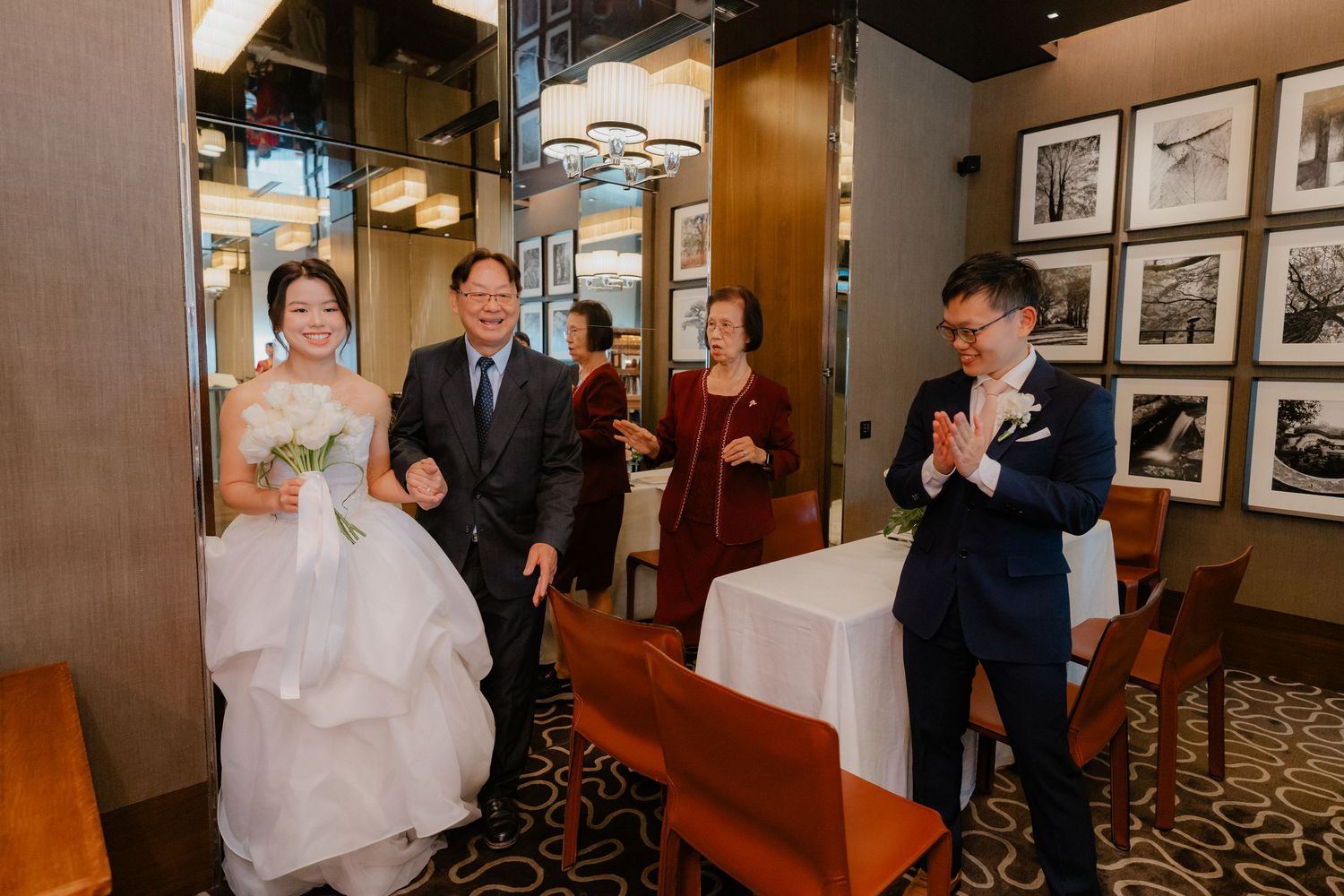 Wedding party walks through an upscale restaurant with black and white photos decorating the wood-paneled walls.