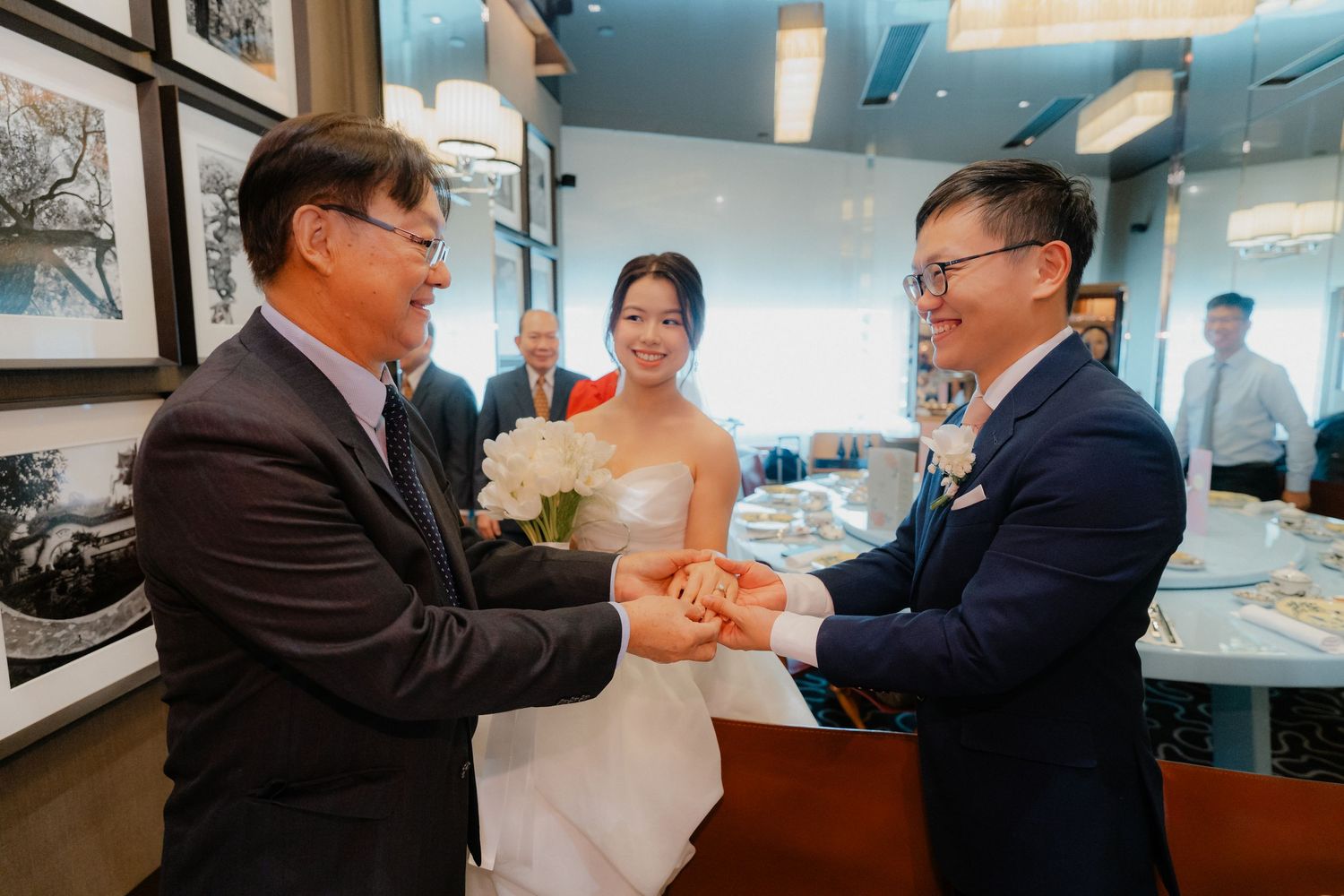 A wedding ceremony takes place in an indoor venue with light blue walls and framed artwork.