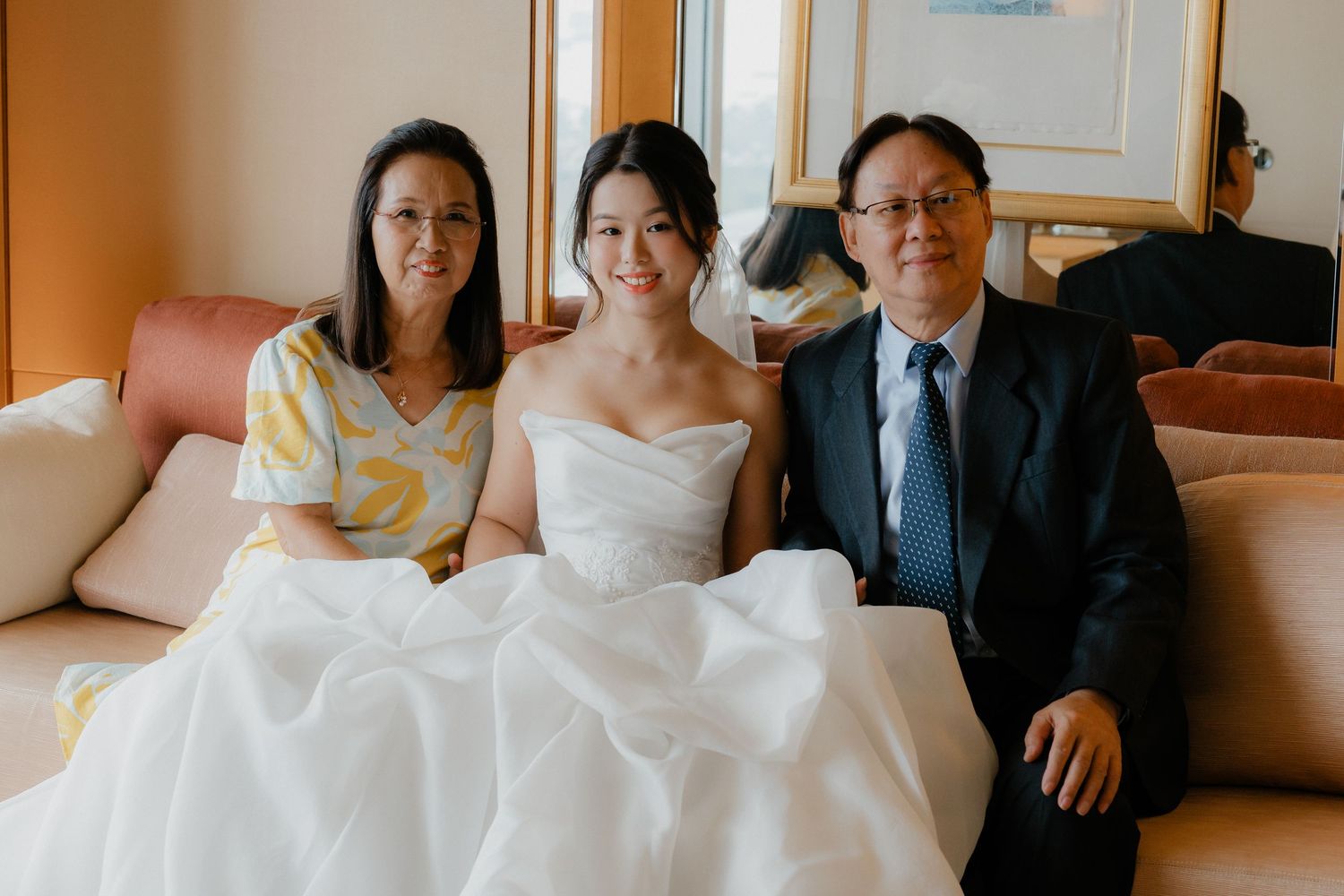 Wedding preparations in a sunlit hotel room showing bride in white dress with family.