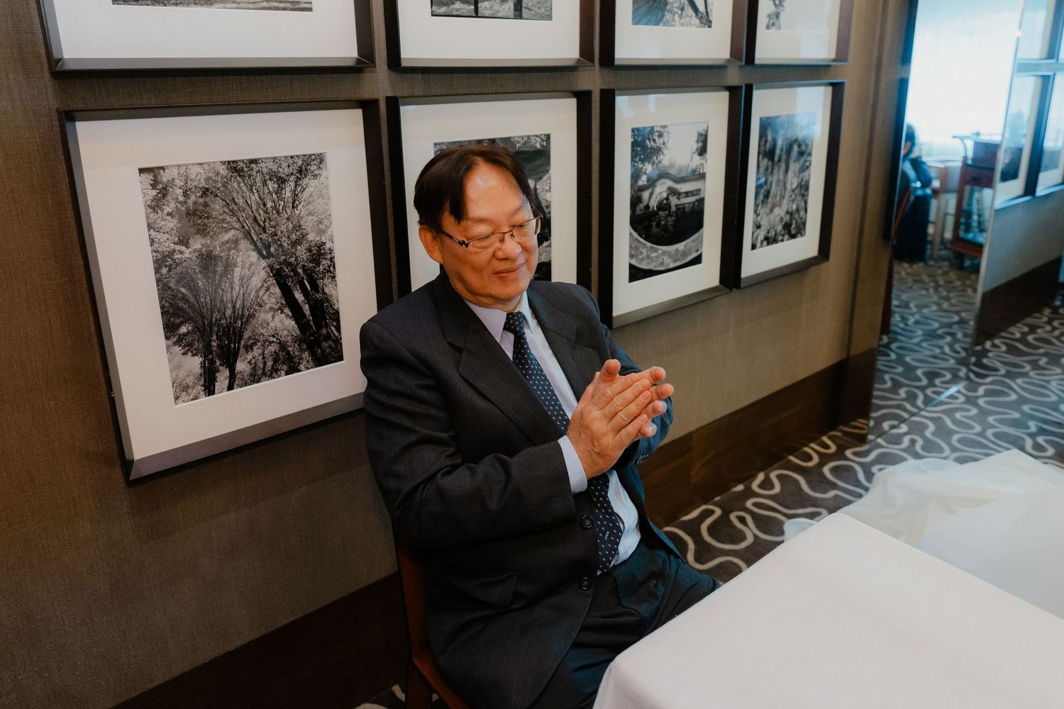 A guest in formal attire seated by a wall of black and white framed photographs.