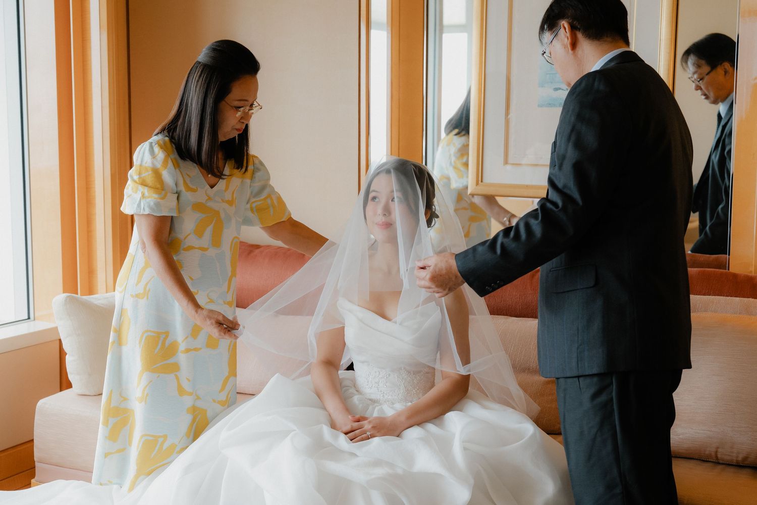 Wedding preparation scene in hotel room with veil being arranged.