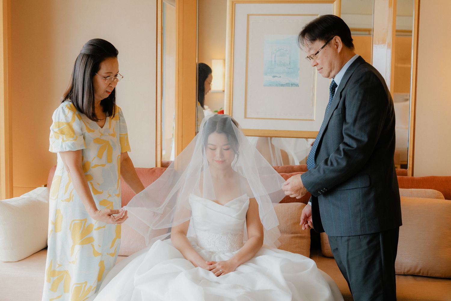 Two people stand in a warmly lit hotel room during wedding preparations.