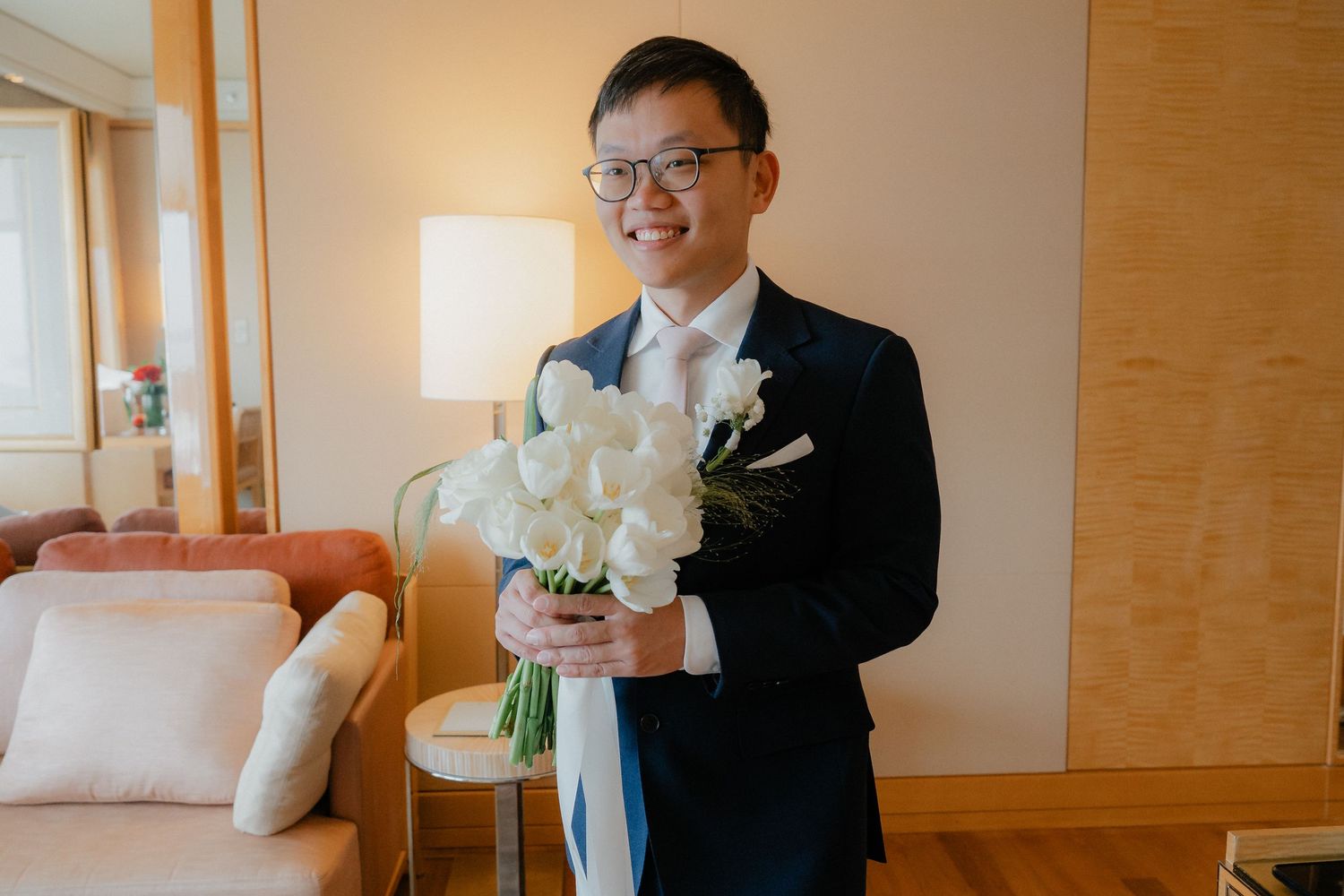 A couple in formal attire share a quiet moment in a sunlit hotel room.