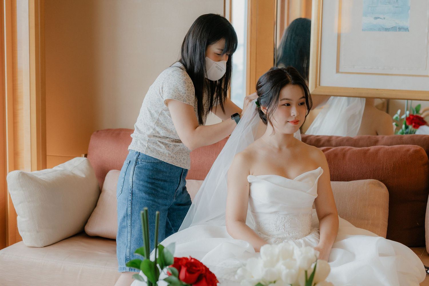 Wedding preparations in a hotel room with white bridal gown and red bouquet.