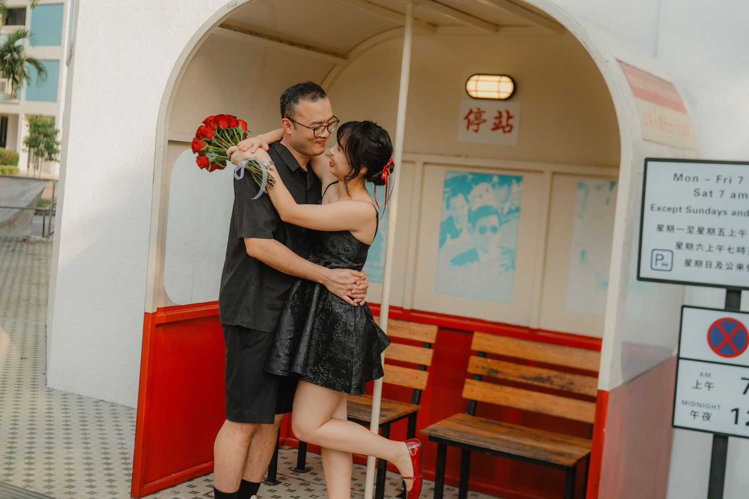 A romantic embrace under a white archway with red roses and a wooden bench.
