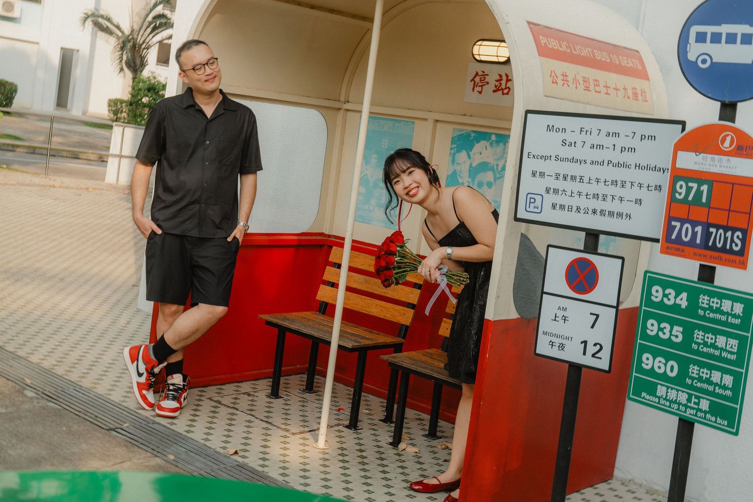 A casual couple relaxes at an outdoor bus stop area with signage in an urban setting.