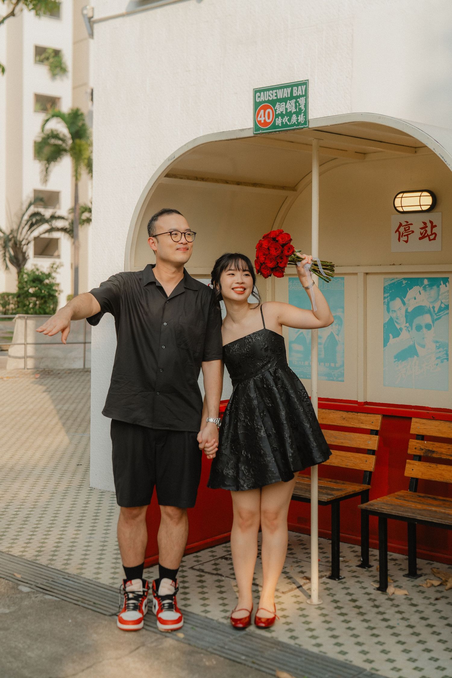 A stylish couple poses outside a retro building with red roses and casual urban attire.