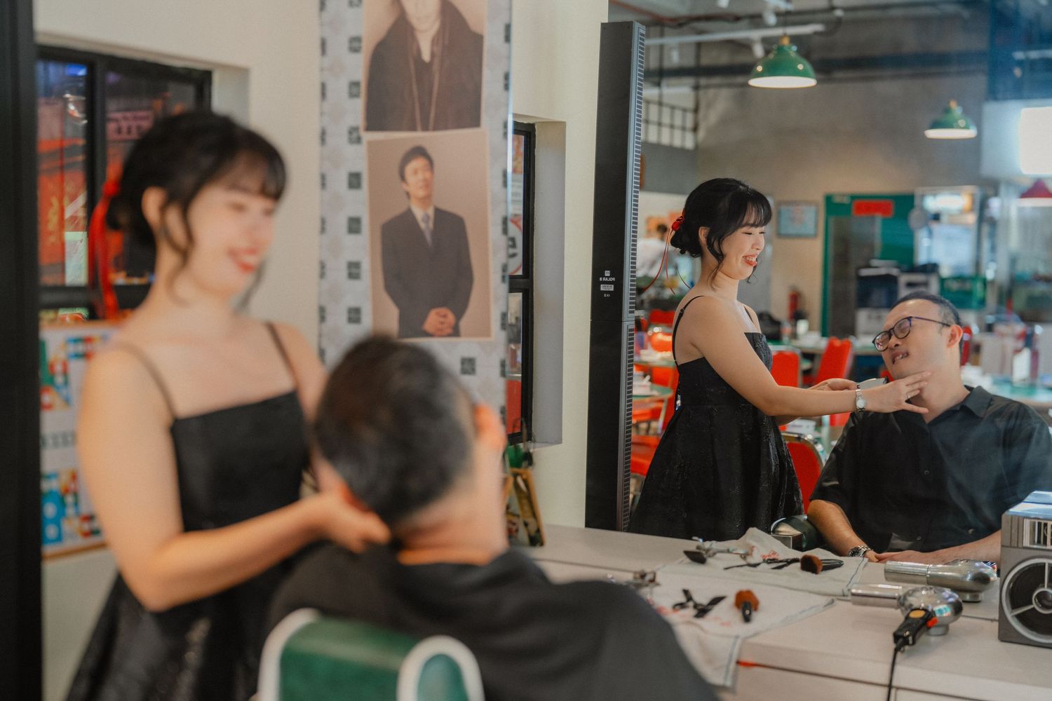 Hairstylist in black dress styles customer's hair while standing at a salon station with a mirror and styling tools.