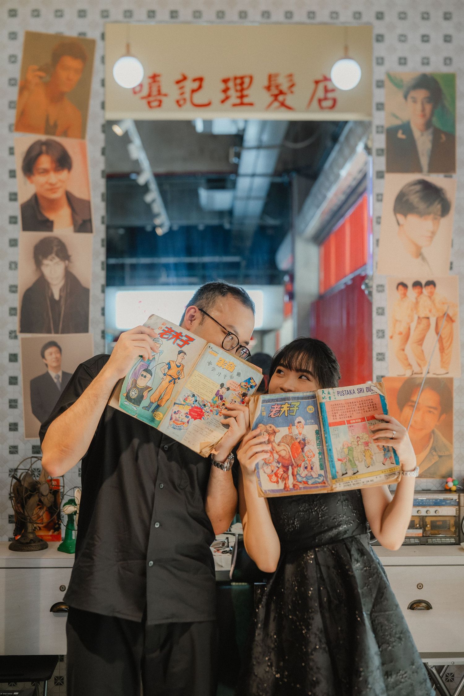 A couple holds up comic books to hide their faces in a retro-themed shop setting.