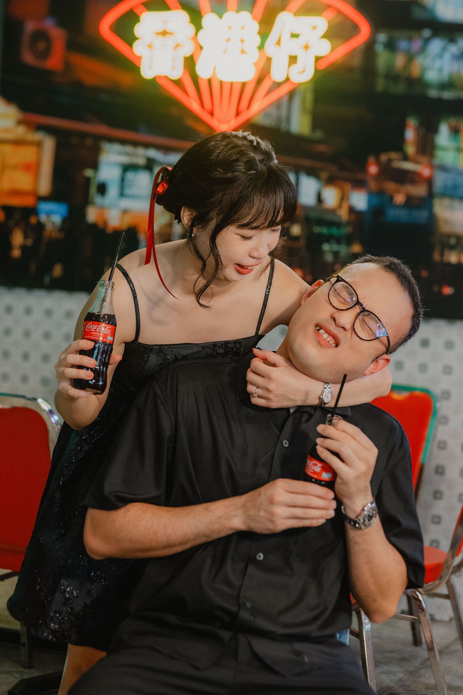 A couple sharing drinks together at a neon-lit restaurant while looking into each other's eyes.