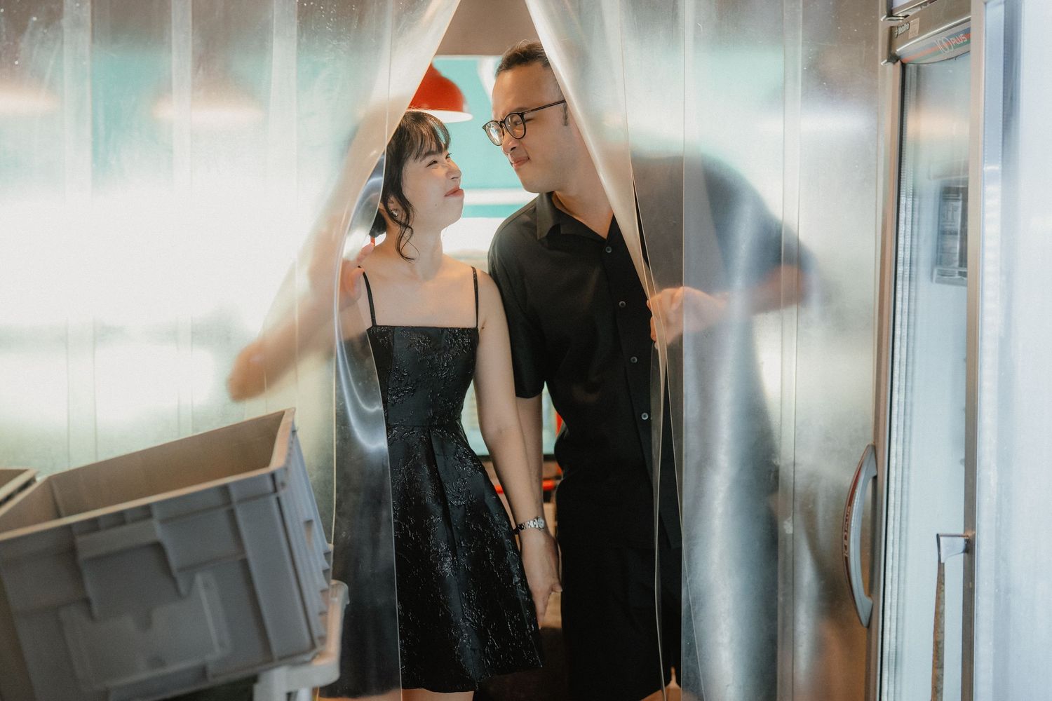 A stylish couple in black outfits share an intimate moment in a bright, modern setting.