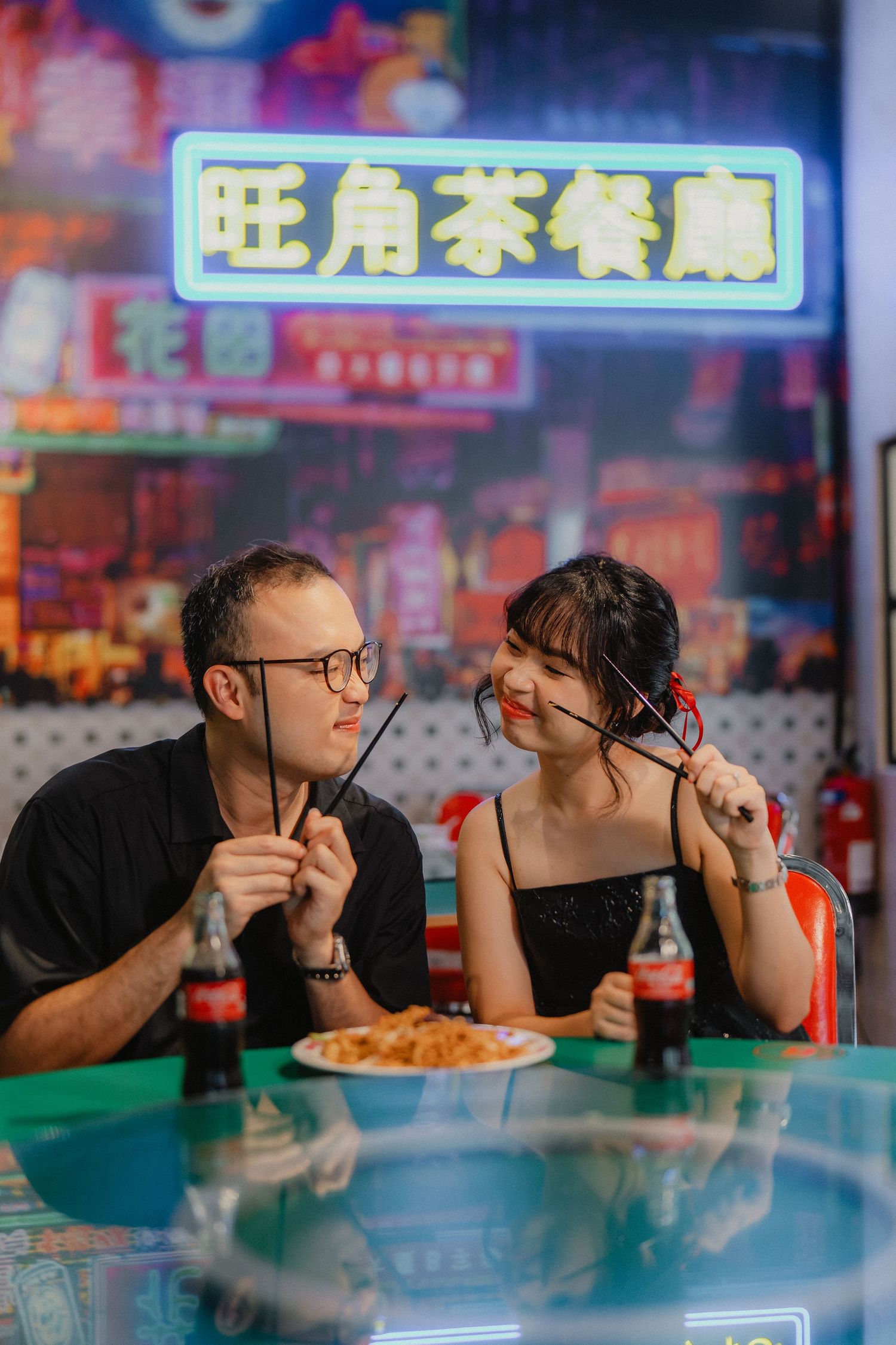 A romantic dinner scene at an Asian restaurant with colorful neon signs in the background.