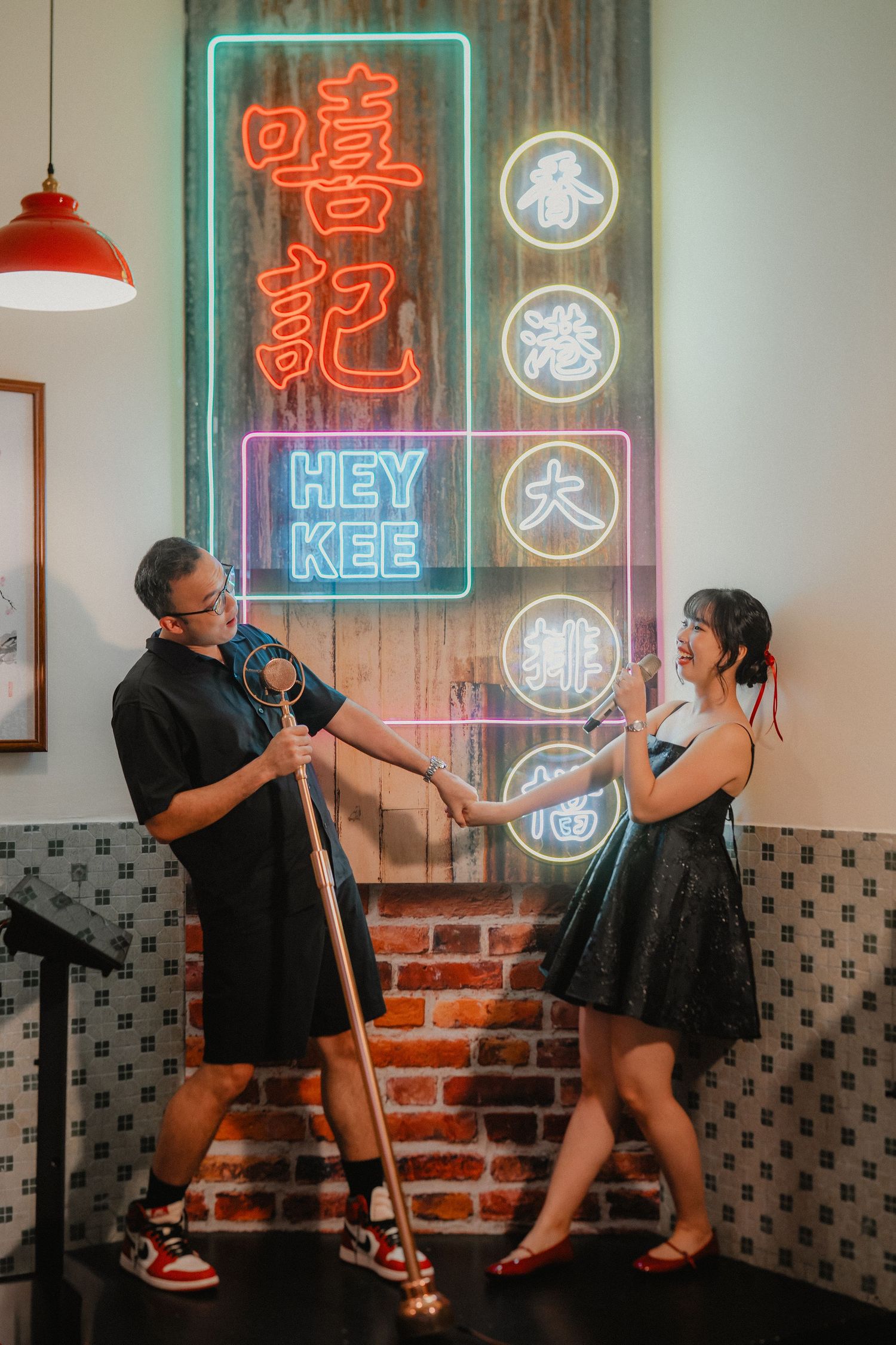 A playful couple poses in front of neon Chinese characters and signs at an Asian restaurant.