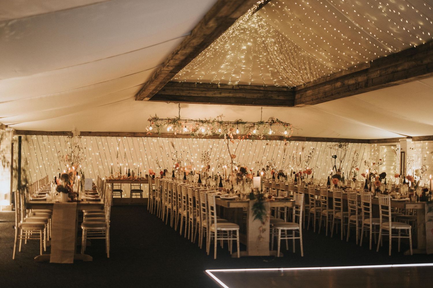 A wedding reception setup with elegant chandeliers and rustic wooden elements in a spacious indoor venue.