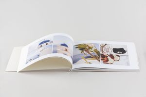 Four identical images showing an open white catalog or photo book lying flat at different angles in studio lighting.