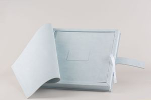 A light blue linen photo album or memory book with delicate craftsmanship lies open on white surface.