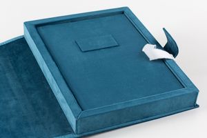 A luxurious teal velvet book or photo album with a decorative bow closure on white background.
