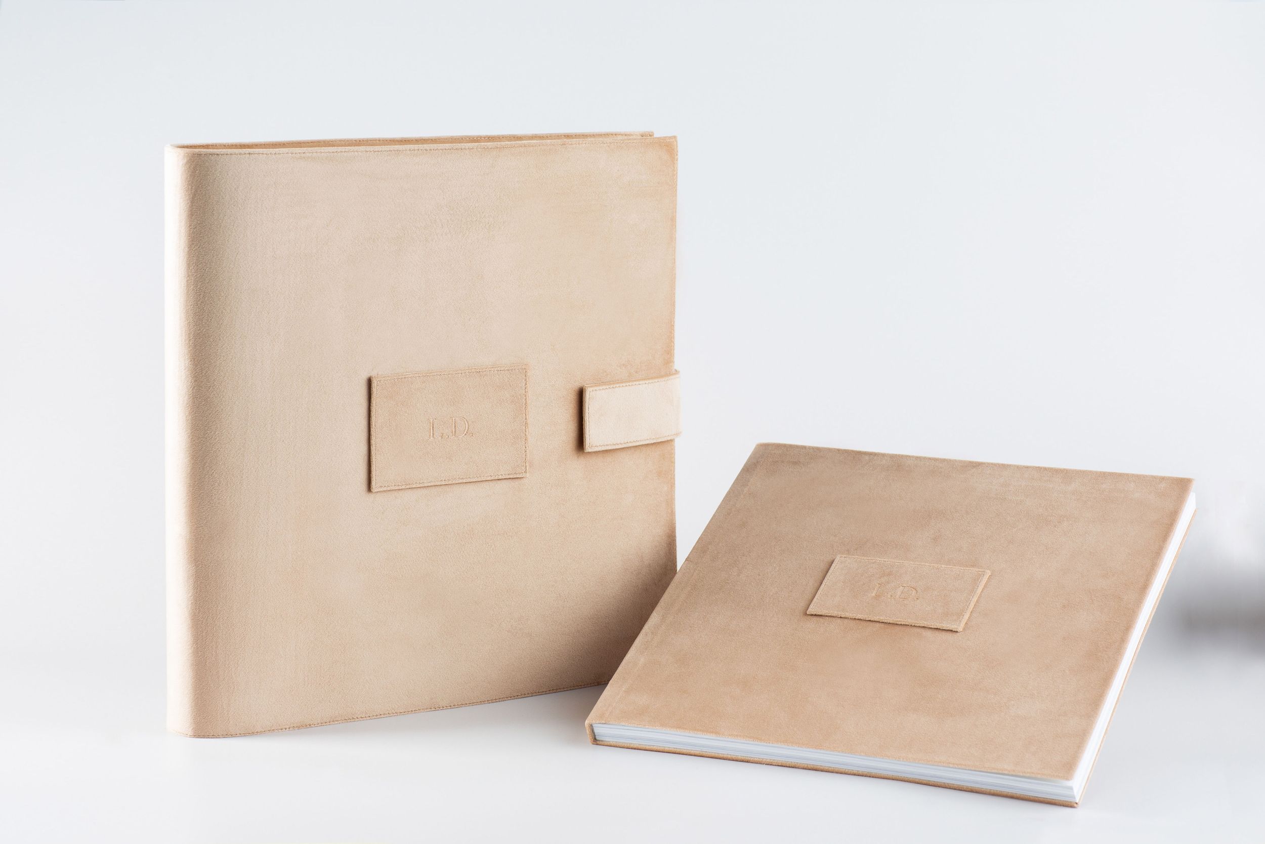 Two minimalist beige leather photo albums with rectangular label patches displayed on white surface.