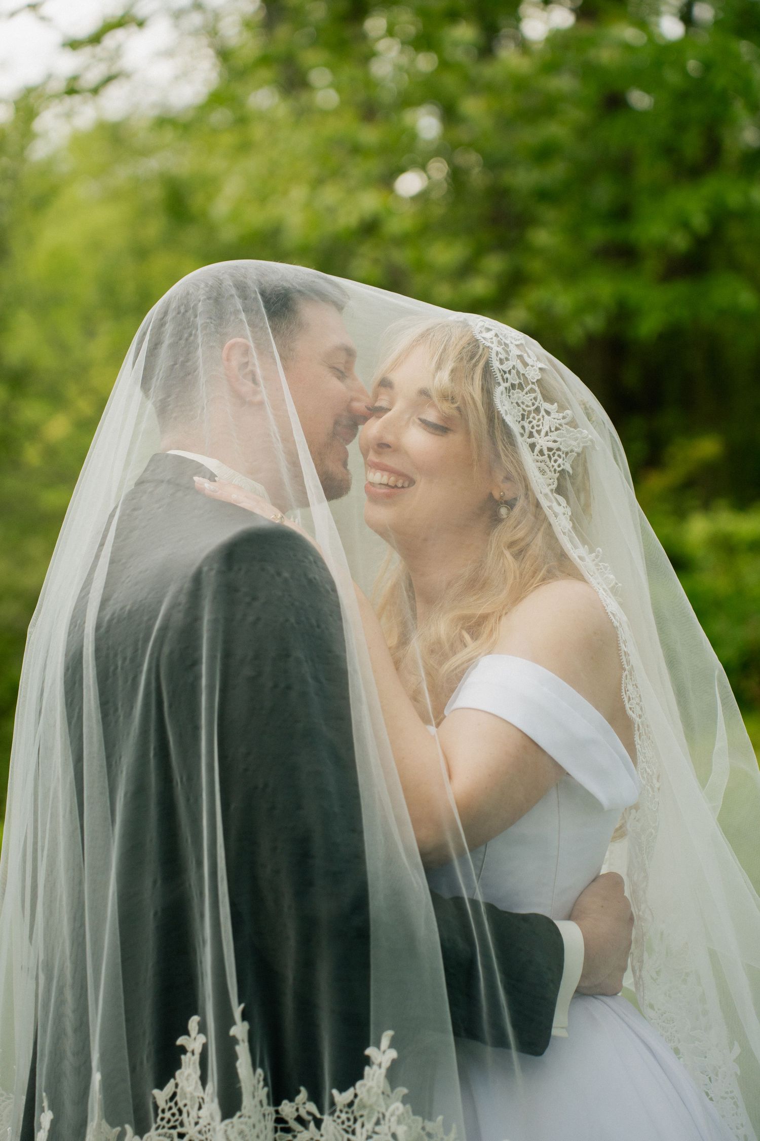 A romantic wedding couple shares intimate moments under a flowing white veil in a garden setting.