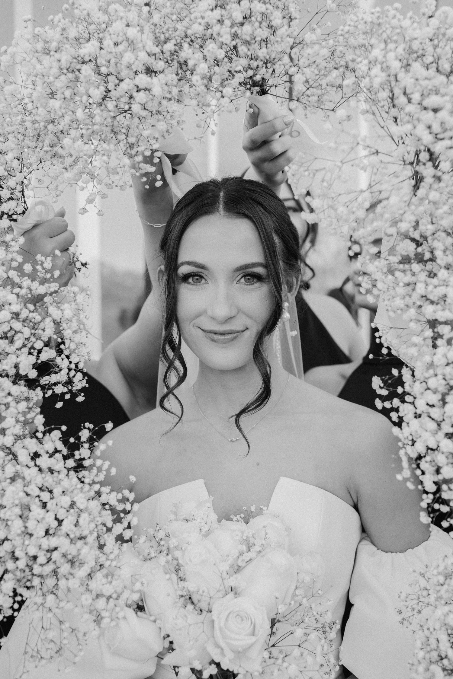 A bride stands amidst delicate cherry blossoms holding a beautiful white bouquet in this dreamy black and white photo.