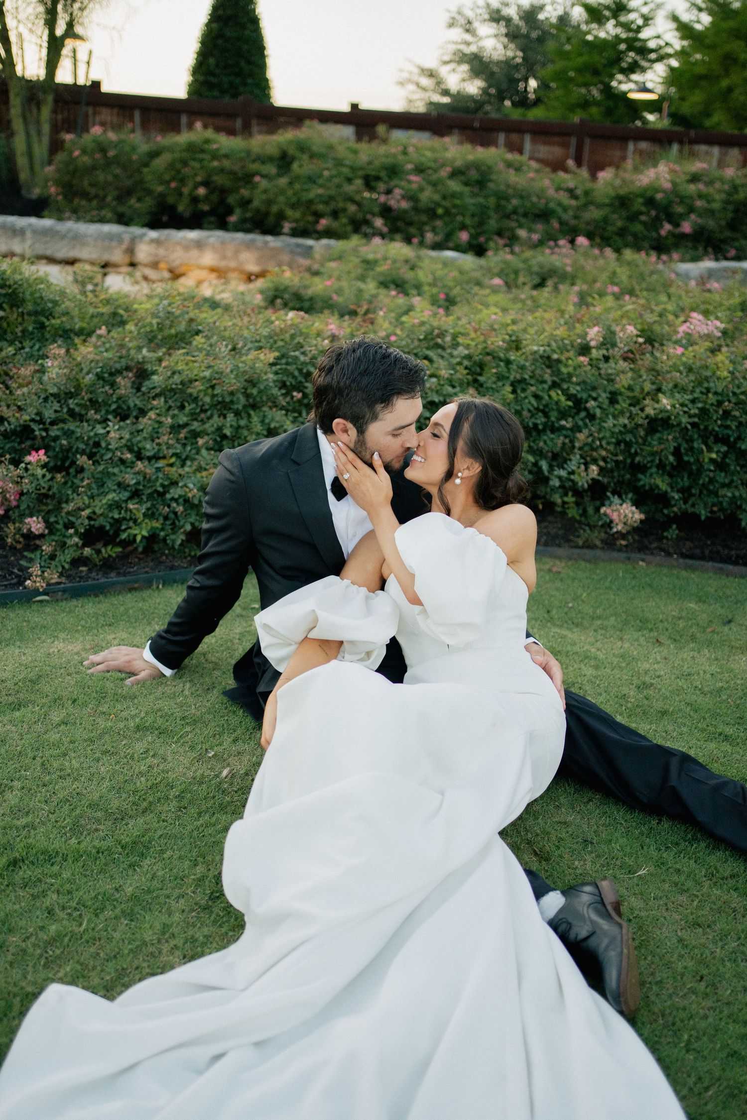 A romantic wedding photo in a garden features a couple in formal attire sharing an intimate moment on the lawn.