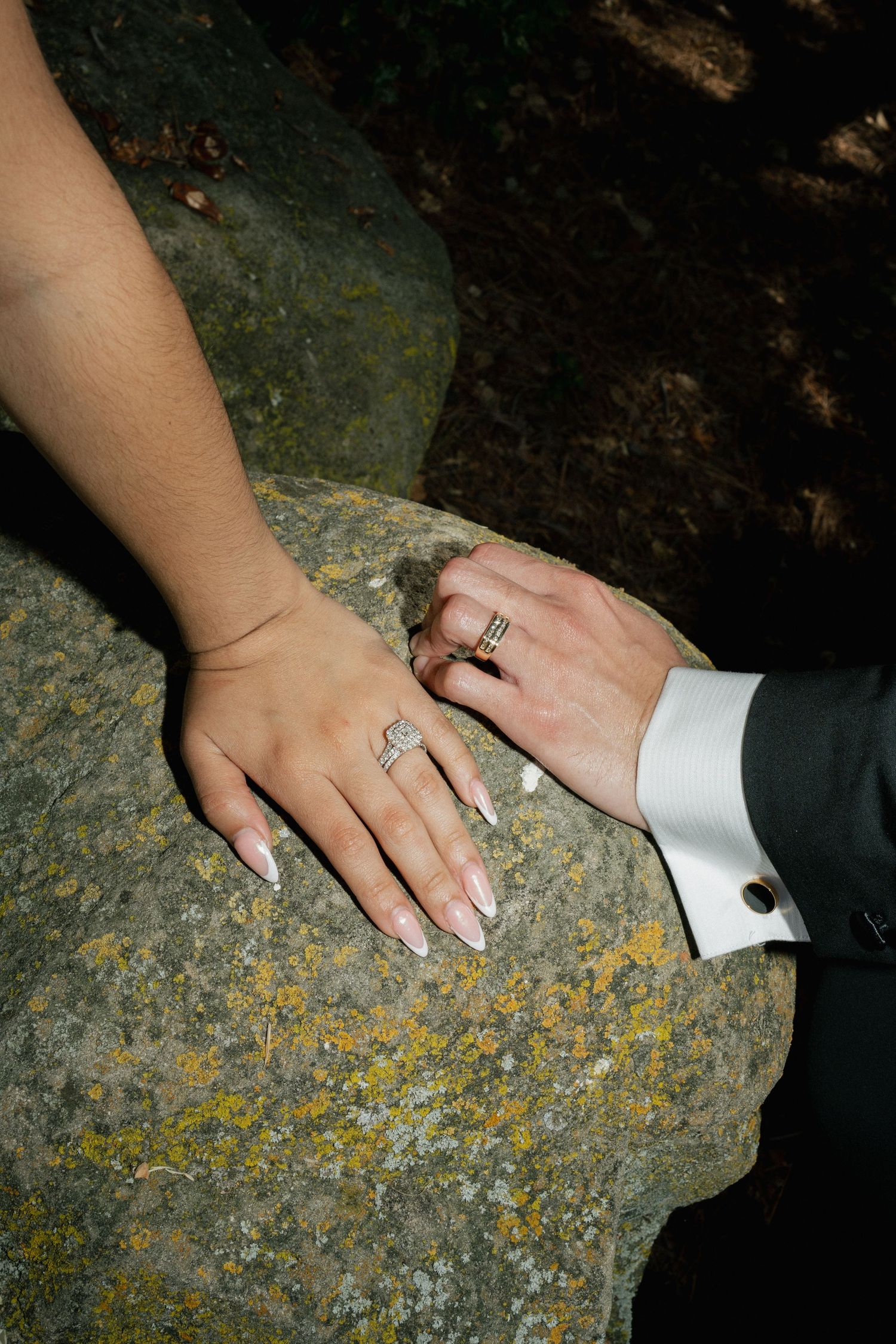 Close up of hands wearing wedding rings resting on a textured stone surface showing newlywed rings details.