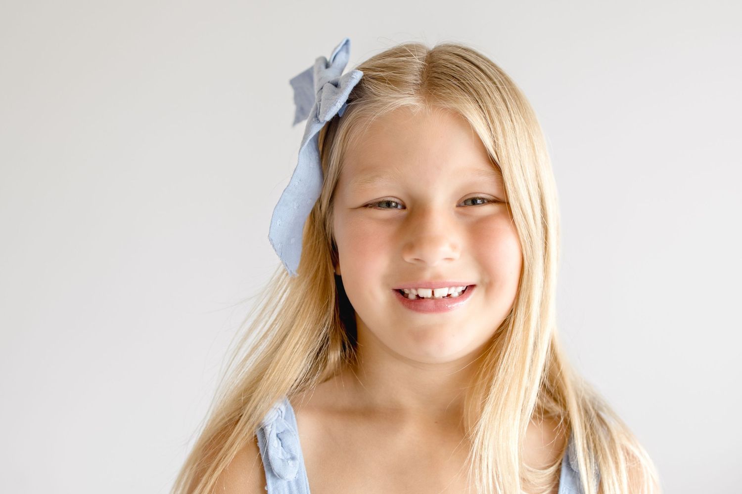 Sweet candid portraits with light blue bow accessory against white backdrop.