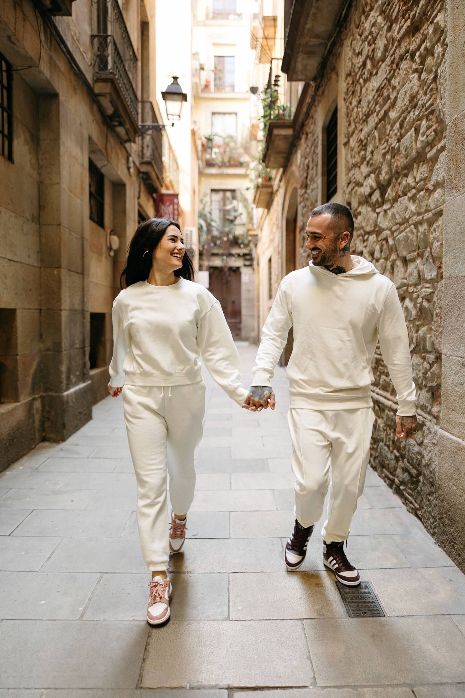 Couple holding hands while walking through narrow European stone alley in matching white outfits.