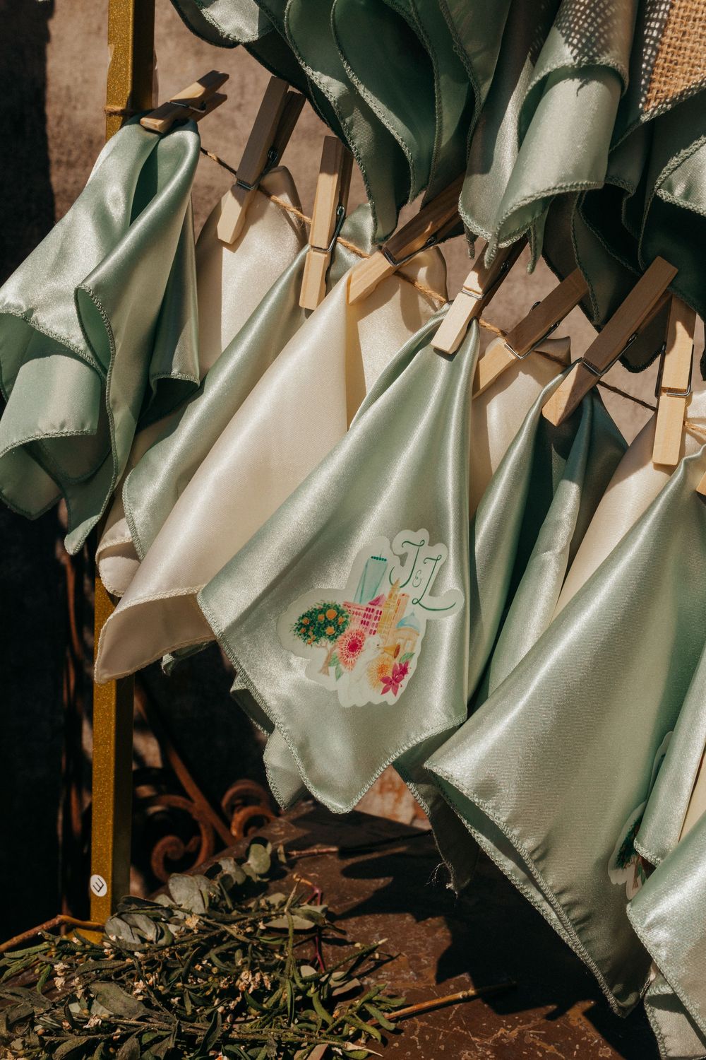 White and sage green fabric napkins with floral embroidery hang from wooden clothespins on a rustic line.