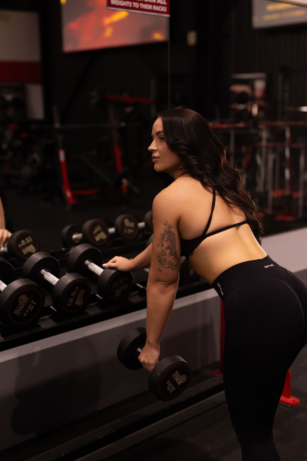 Fitness enthusiast performs a single arm row exercise with dumbbells on a bench in a dimly lit gym setting.