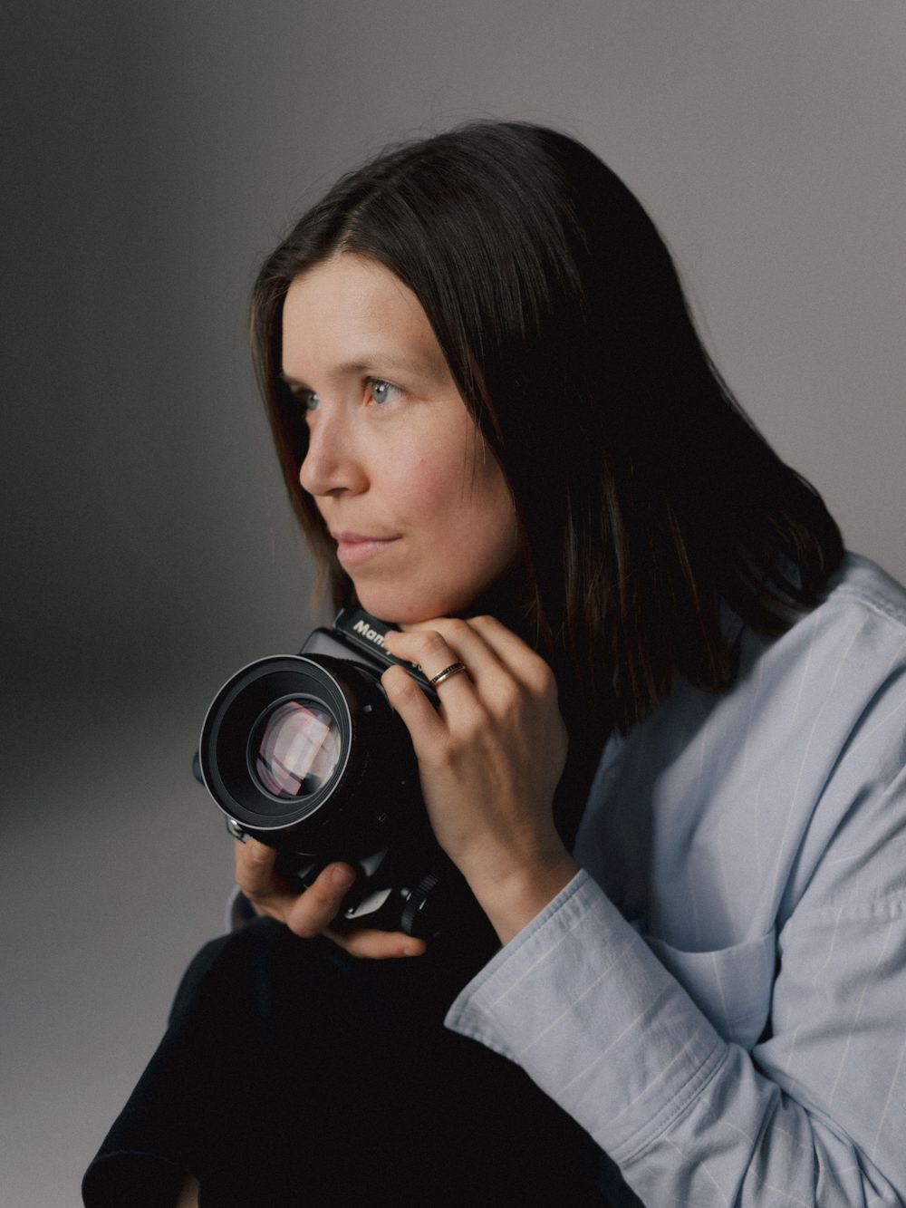 Photographer wearing a light gray sweater holds a professional camera while composing shots from different angles.