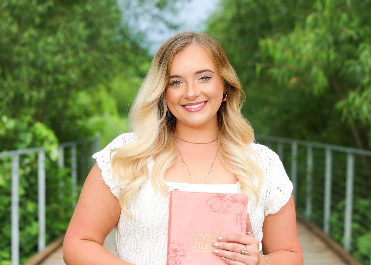 Styled outdoor portrait session feat a woman holding her Bible while surrounded by green foliage in Osage Park Bentonville AR