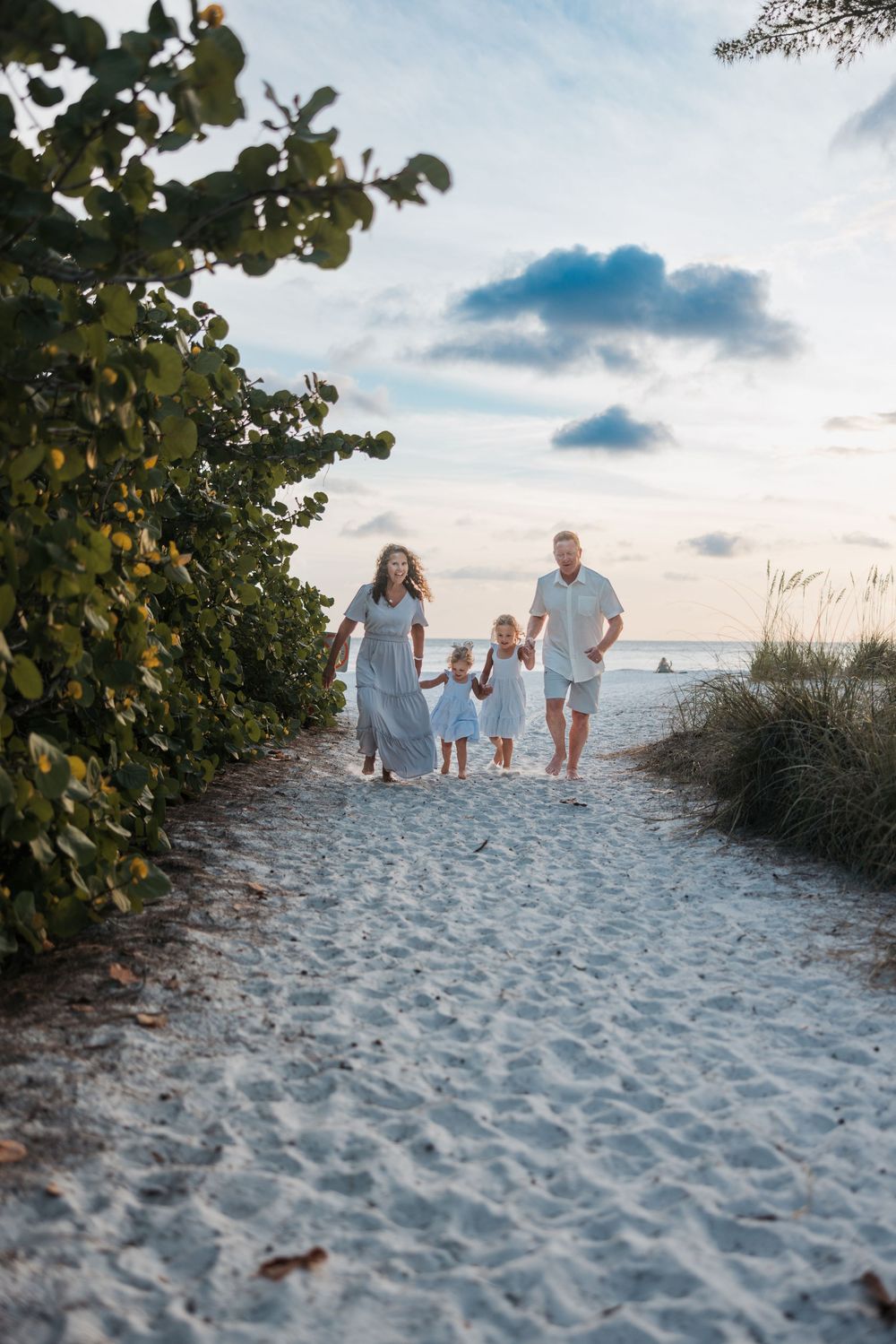 People walking up a sandy pathway flanked by sea grapes leading to a beach at sunset.