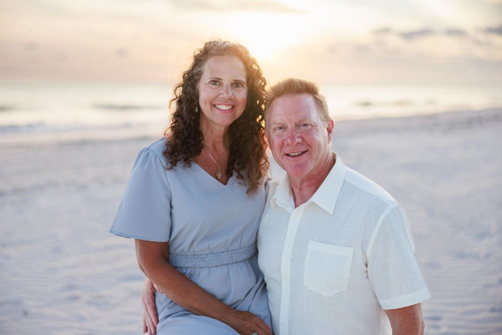 Couple posing together at sunset on a beach with cloudy sky in the background.